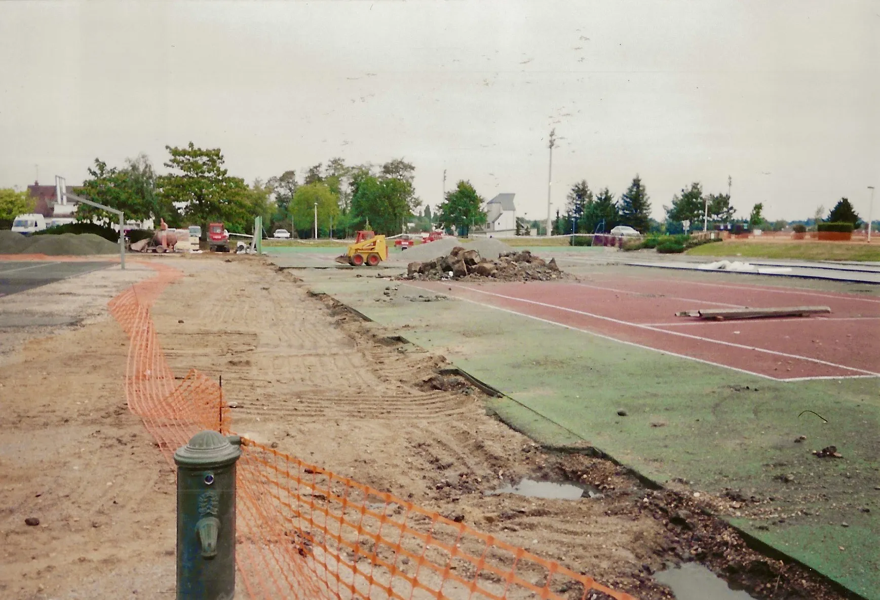 Travaux de démolition et de rénovation d’un court de tennis, incluant l’enlèvement des anciennes couches et la préparation du sol pour un nouveau revêtement en béton poreux.