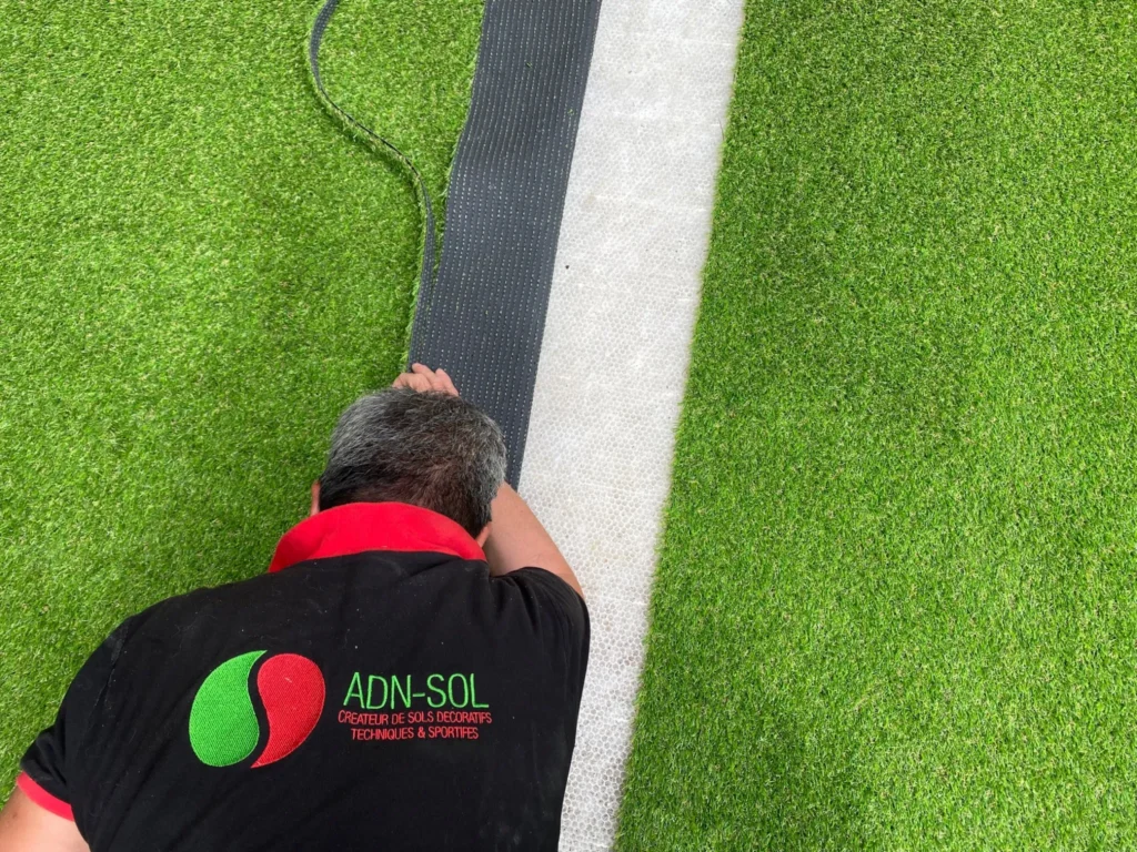 Installation de pelouse synthétique sur un court de tennis par un technicien ADN-SOL