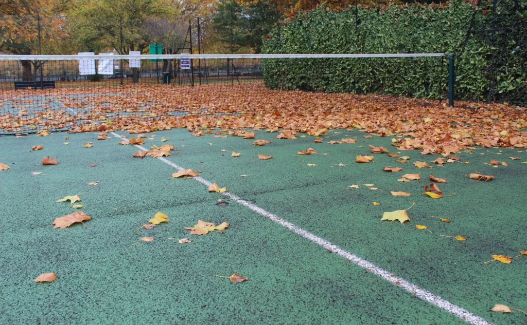 Court de tennis extérieur usé et envahi par les feuilles à l’automne, nécessitant une rénovation