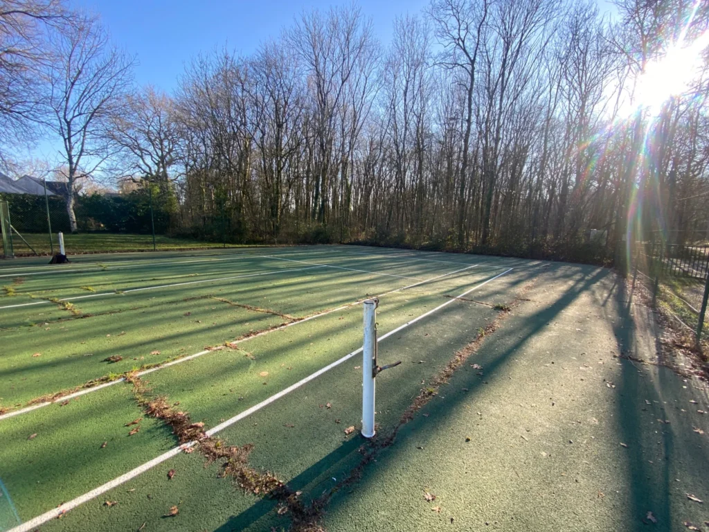 Court de tennis avant rénovation avec revêtement usé nécessitant une estimation des travaux