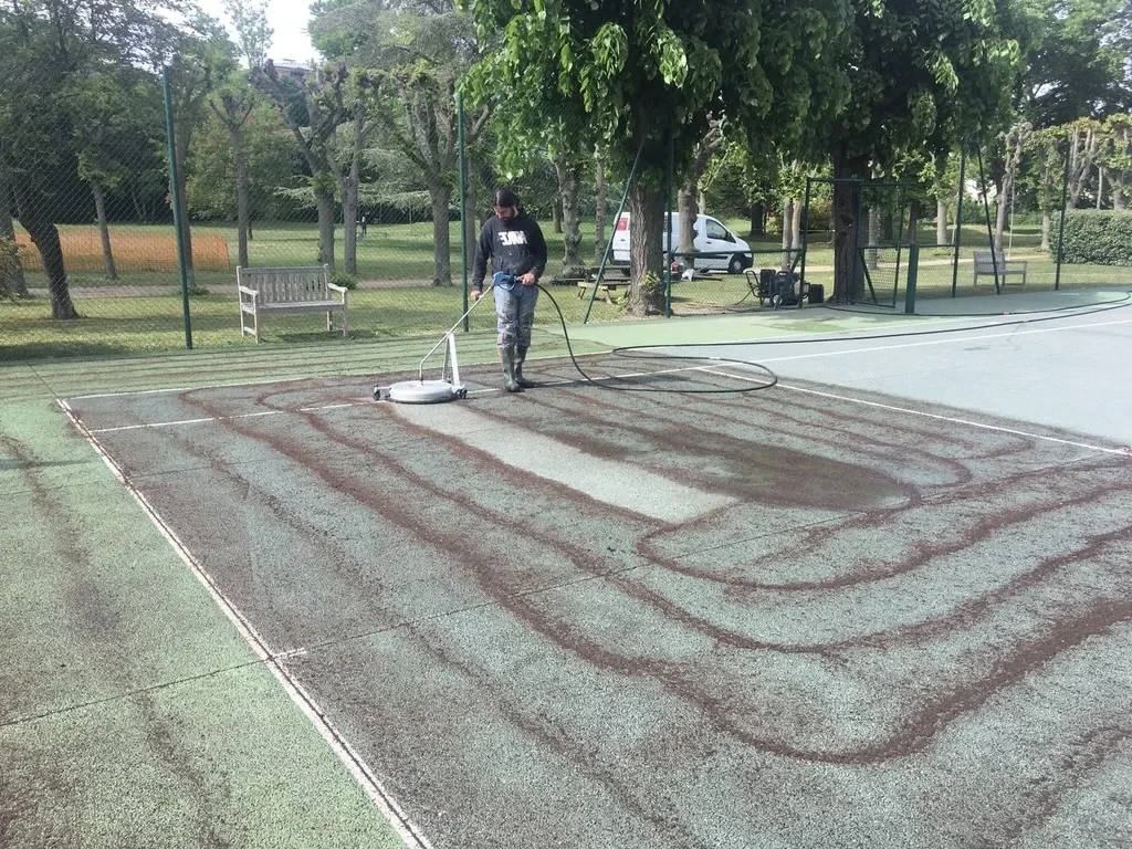 Nettoyage d'un court de tennis avant resurfaçage à l'aide d'un nettoyeur haute pression avec cloche rotative pour préparer le revêtement avant rénovation.