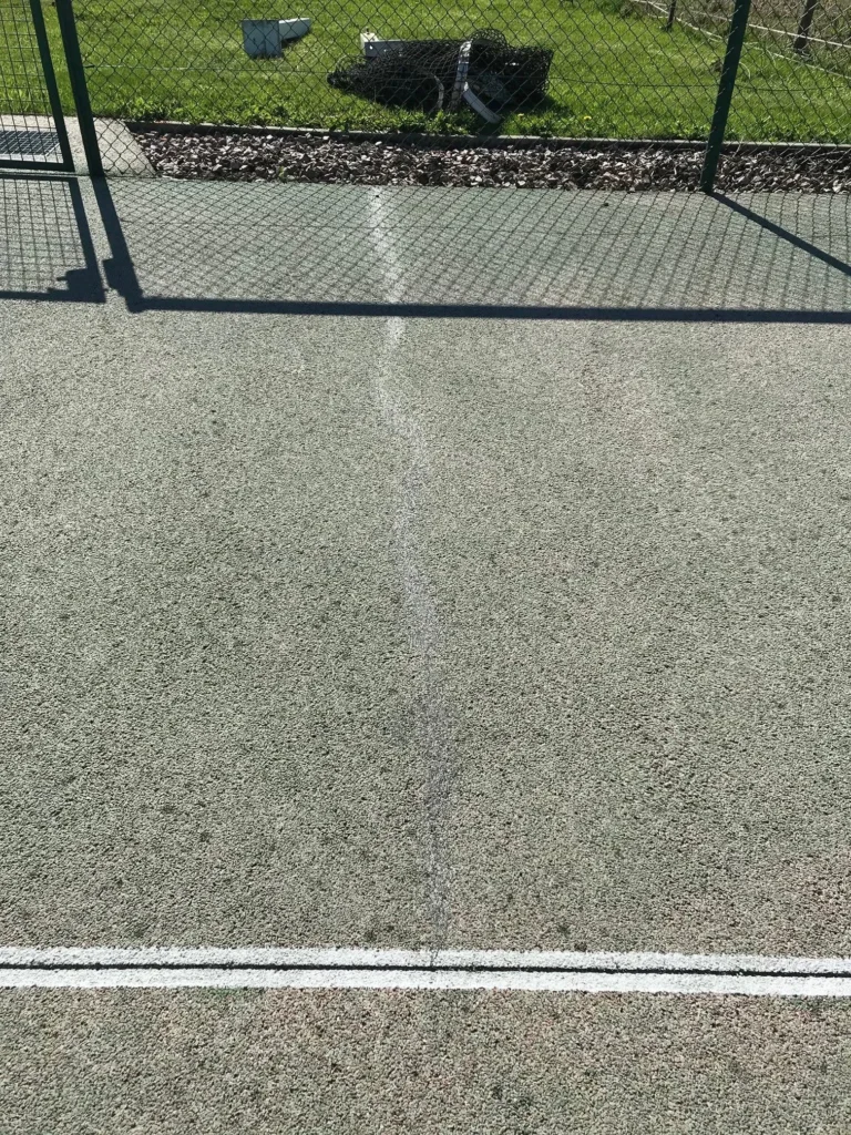 Traitement des fissures avant resurfaçage d'un terrain de tennis en béton poreux afin de stabiliser le support avant l'application du nouveau revêtement.