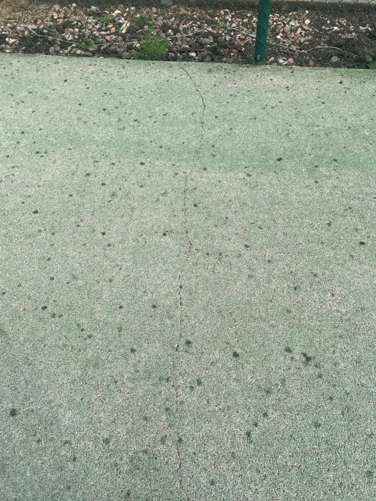 Fissure longitudinale sur un terrain de tennis faisant l'objet d'un traitement avant resurfaçage afin d'assurer une rénovation durable du revêtement.